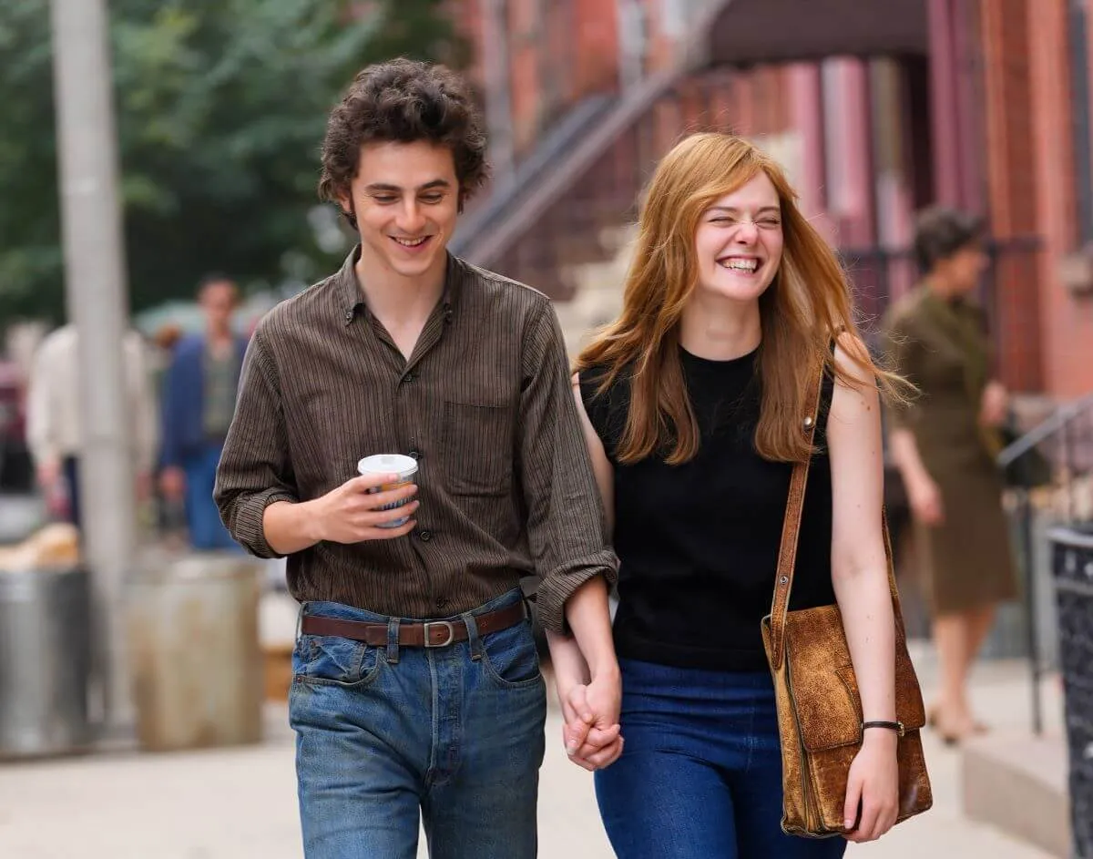 Timothee Chalamet and Elle Fanning hold hands while walking. He holds a coffee and she holds onto her purse.