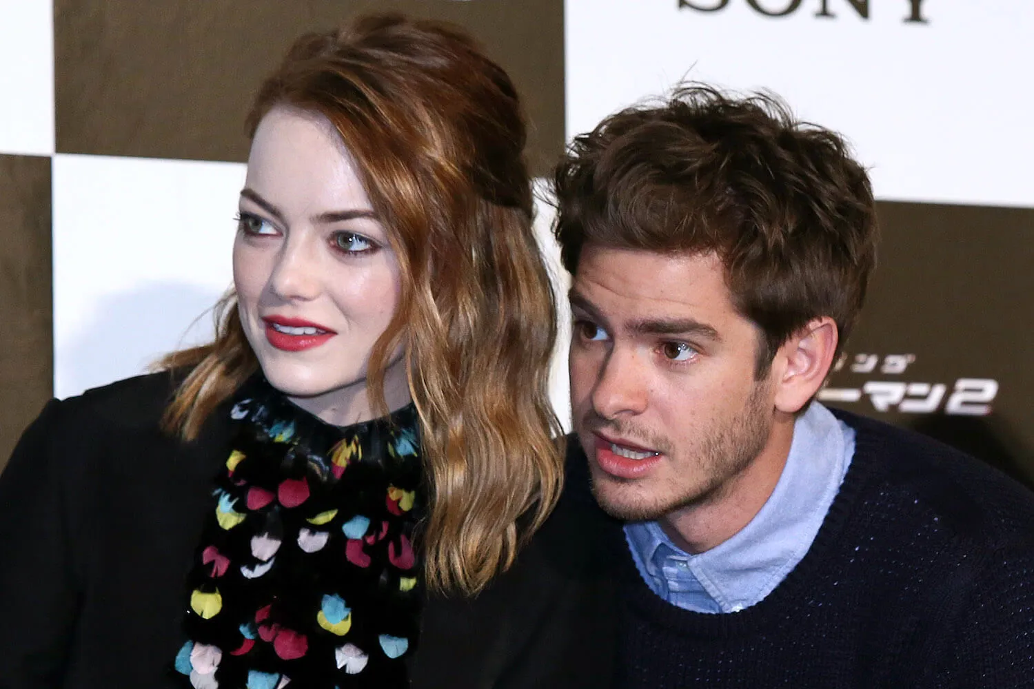 Emma Stone and Andrew Garfield, with their faces close to each other, are looking intently at something to their right.