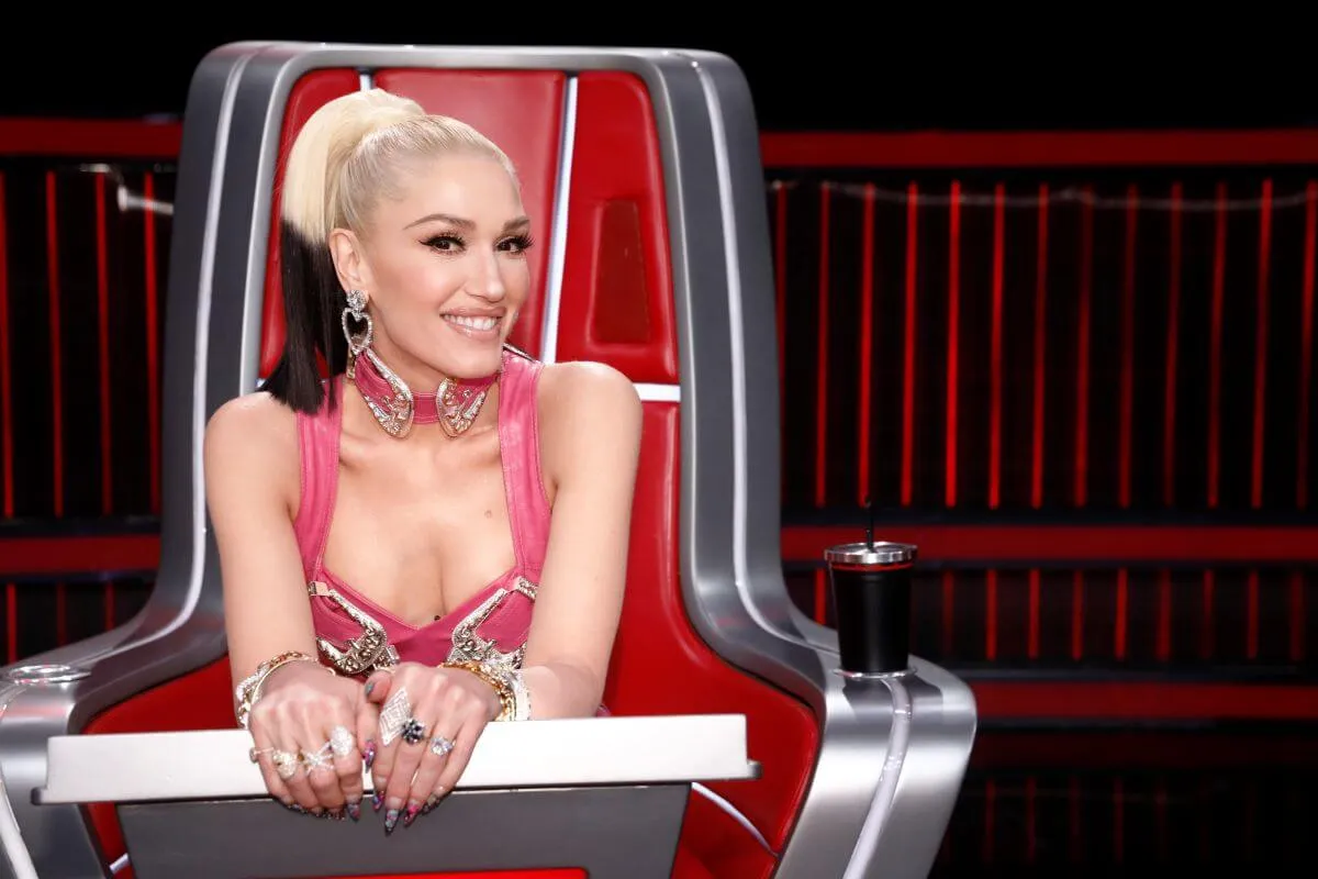 Gwen Stefani wears a pink dress and sits in a chair on 'The Voice.'