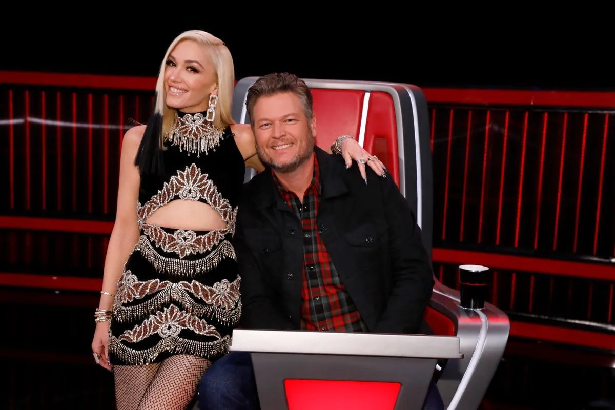 Gwen Stefani perches on Blake Shelton's 'The Voice' Chair. She has her arm around his shoulders.