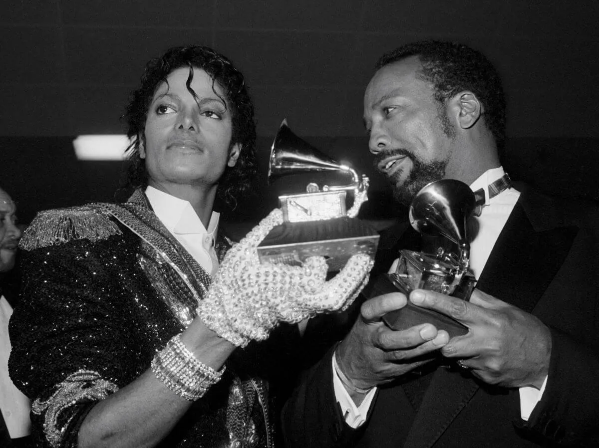 A black and white picture of Michael Jackson and Quincy Jones holding Grammys. Jackson wears sequined gloves.