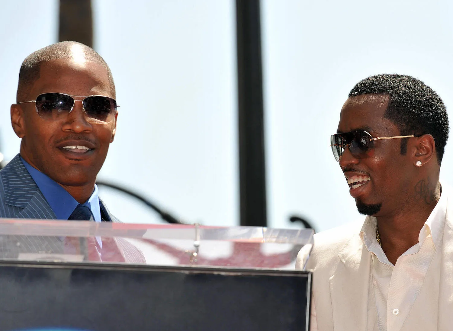 Jamie Foxx speaking at a podium with Sean 'Diddy' Combs smiling next to him