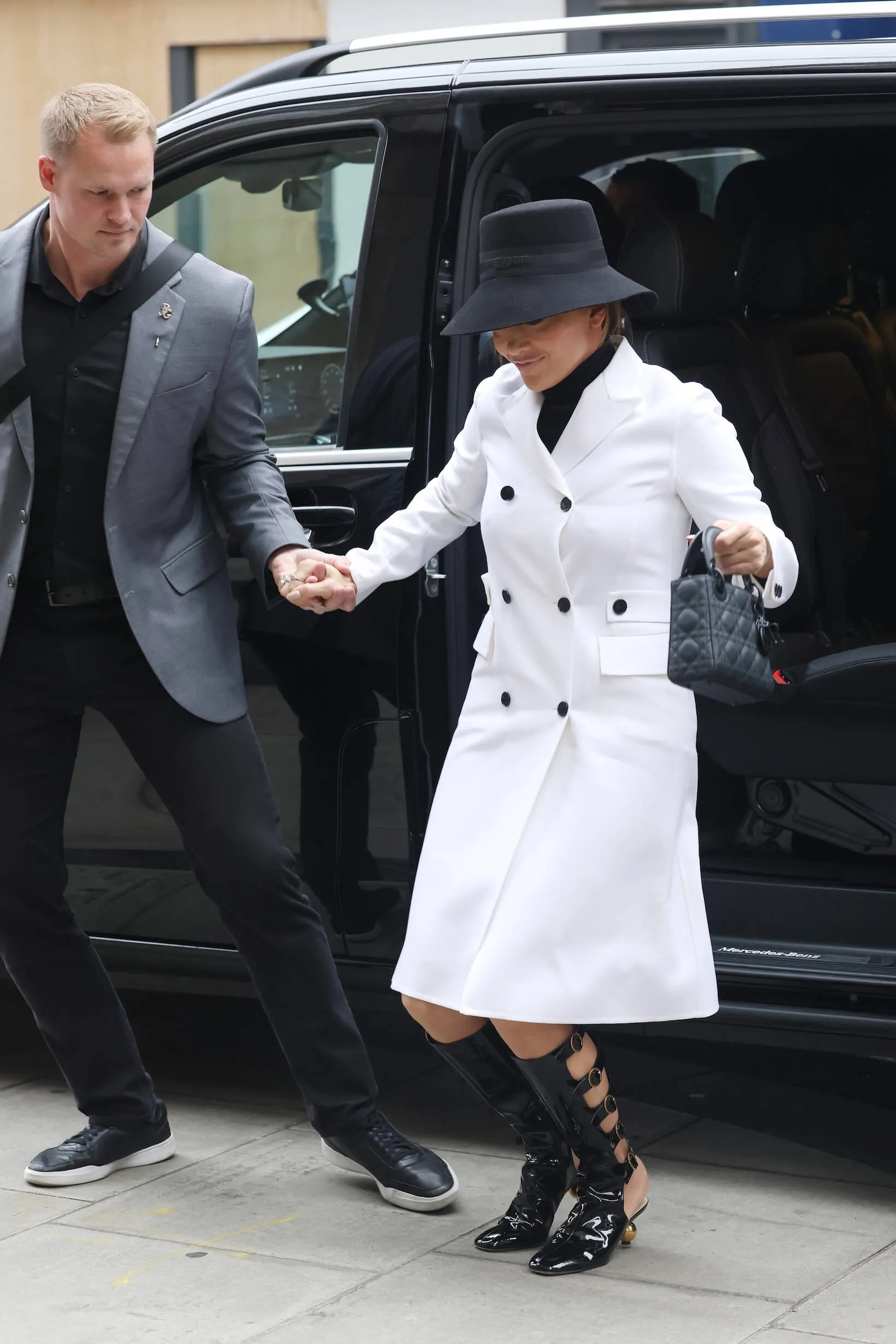 Jennifer Lopez in a white coat stepping out of a black SUV and taking her bodyguard's hand as she steps