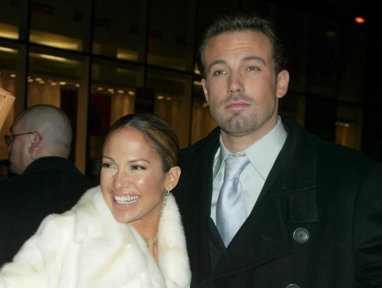 Jennifer Lopez smiling while standing next to Ben Affleck at the 'Maid in Manhattan' premiere afterparty. Lopez is wearing a white fur coat; Affleck is wearing a suit and tie.