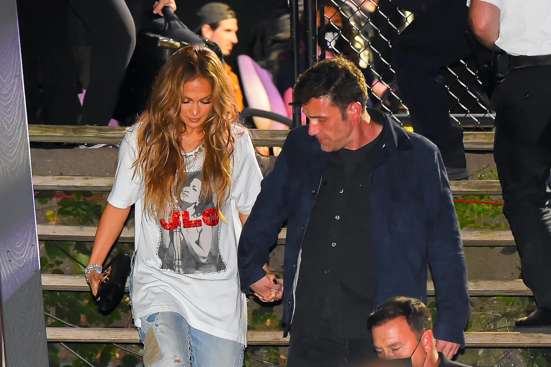 Jennifer Lopez and Ben Affleck holding hands and looking down as they walk down stairs at night in a crowd