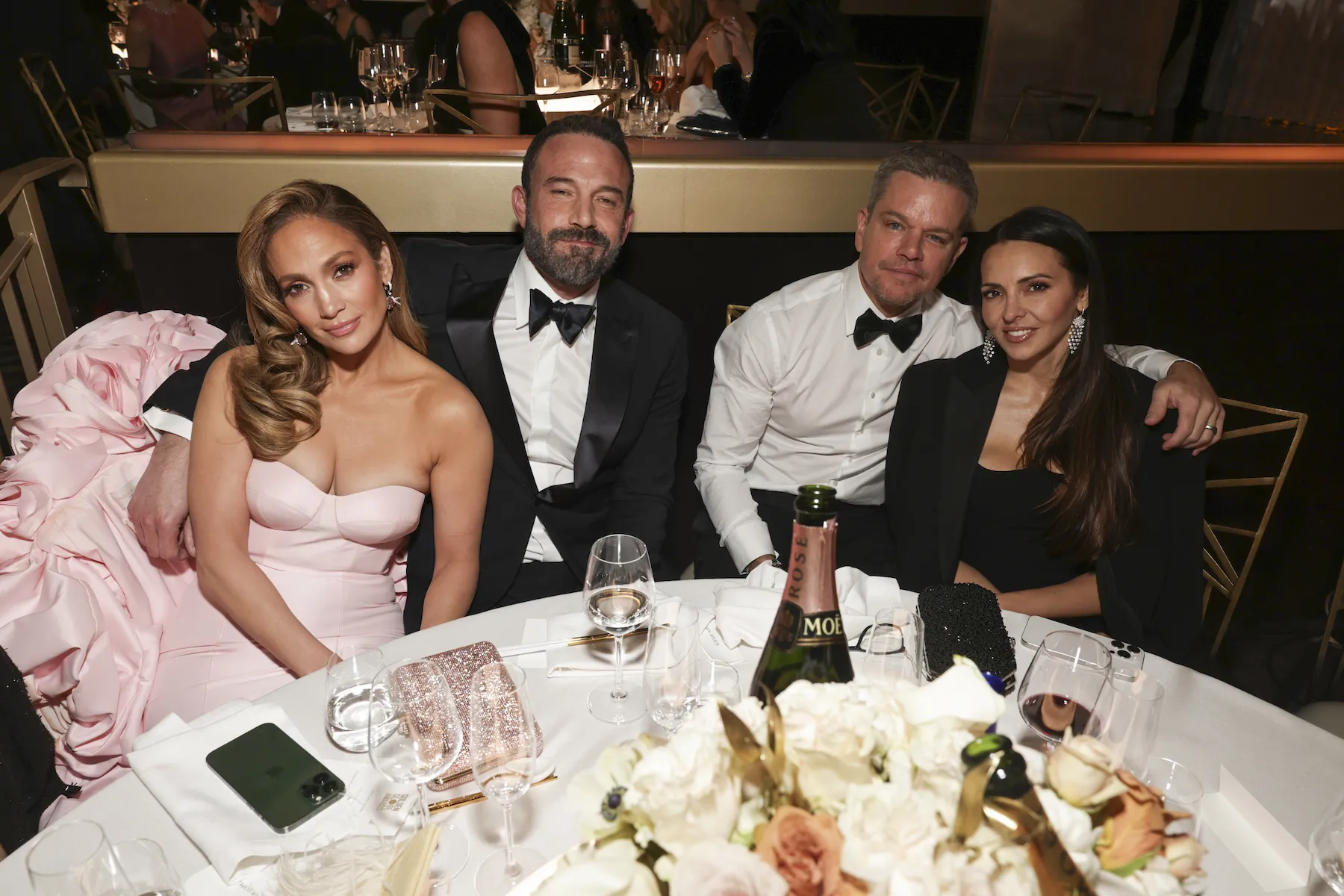 Jennifer Lopez, Ben Affleck, Matt Damon, and Luciana Damon sitting around a table and smiling at the camera at the 81st Golden Globe Awards