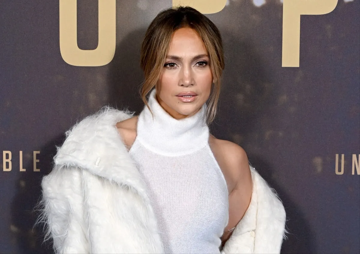 Wearing a white coat and white sweater dress, Jennifer Lopez poses on the red carpet before the UK premiere of 'Unstoppable'