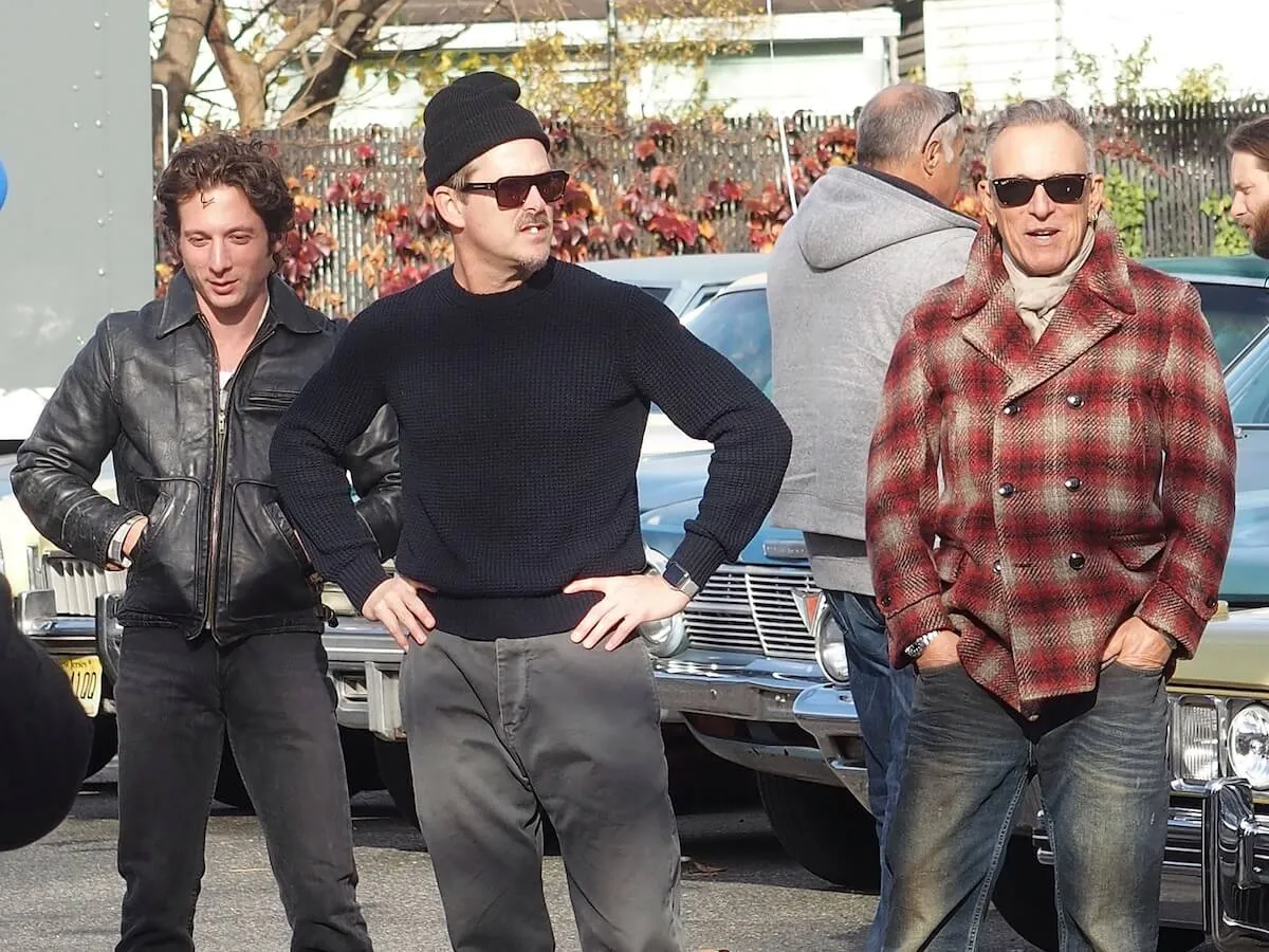 Jeremy Allen White, Scott Cooper, and Bruce Springsteen standing outside in front of old cars