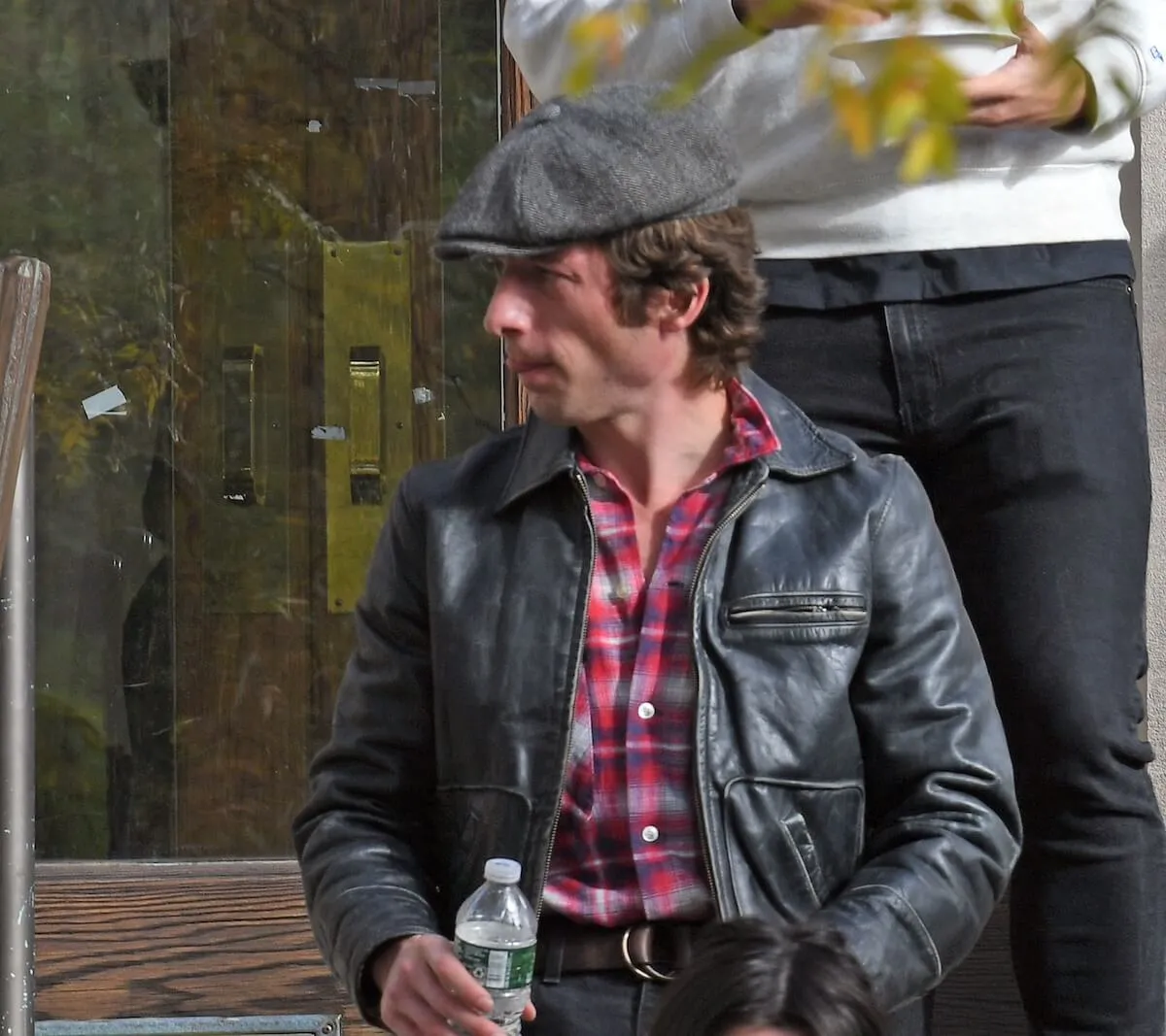 Jeremy Allen white wearing a cap and black leather jacket and holding a bottle of water on the set of Bruce Springsteen biopic