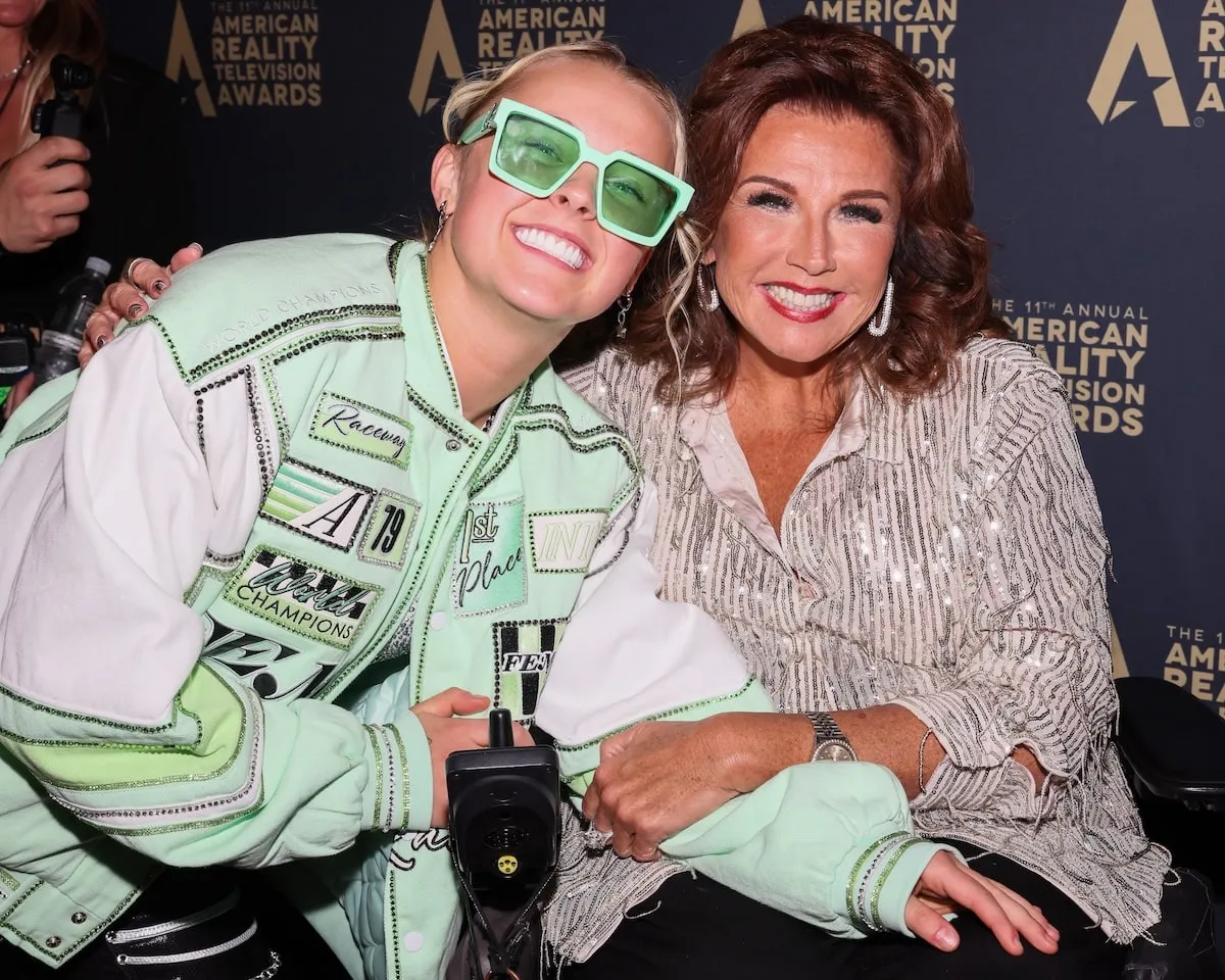 Wearing a mint colored jacket and black shorts, JoJo Siwa smiles with Abby Lee Miller on the red carpet at the 2024 Reality TV Awards