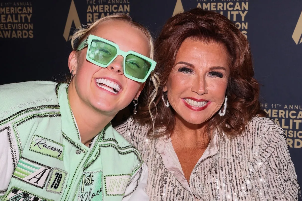 Wearing a mint colored jacket and black shorts, JoJo Siwa smiles with Abby Lee Miller on the red carpet at the 2024 Reality TV Awards