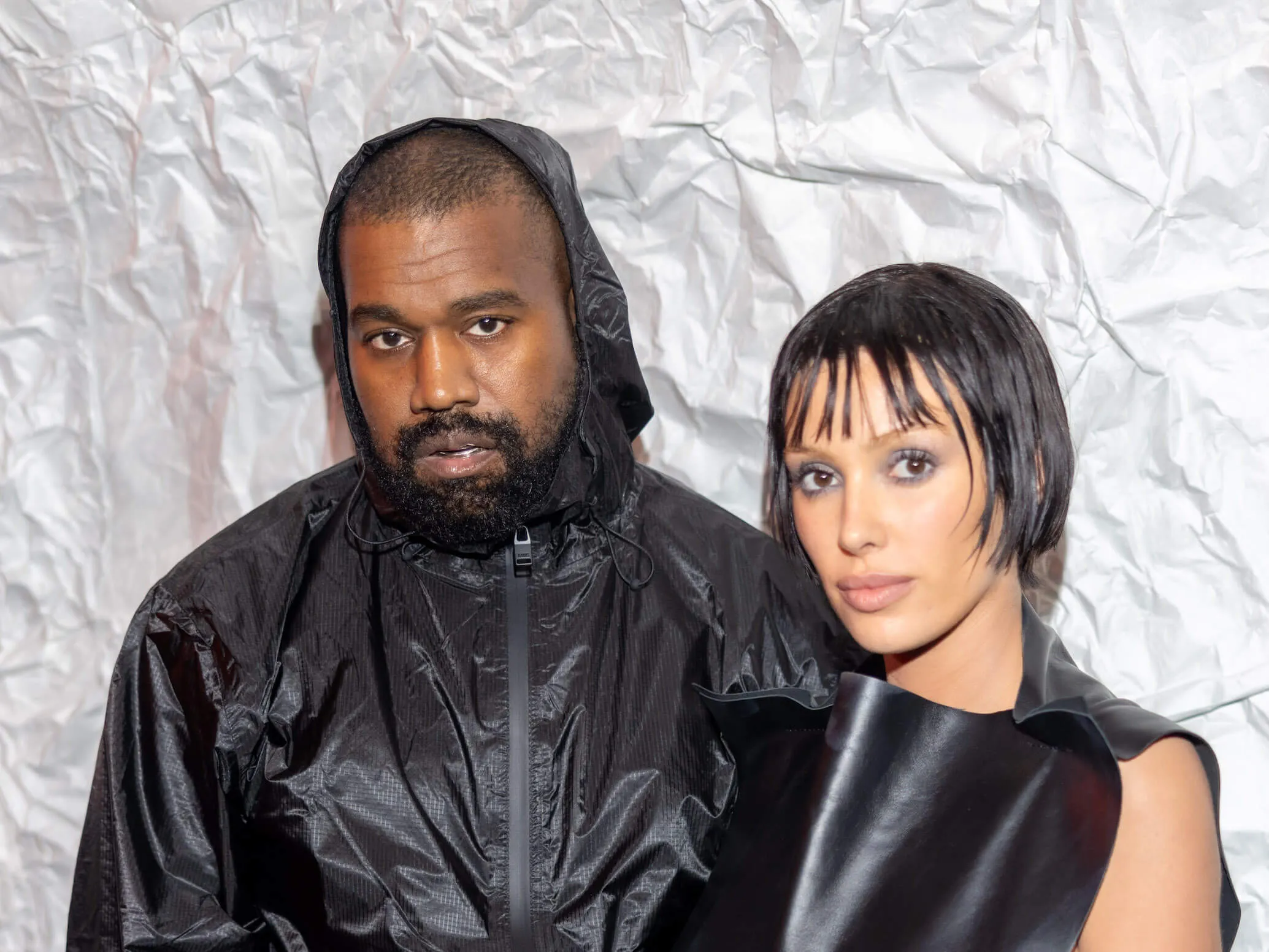 Kanye West and Bianca Censori standing next to each other and posing at Milan Fashion Week. They are both dressed in black.