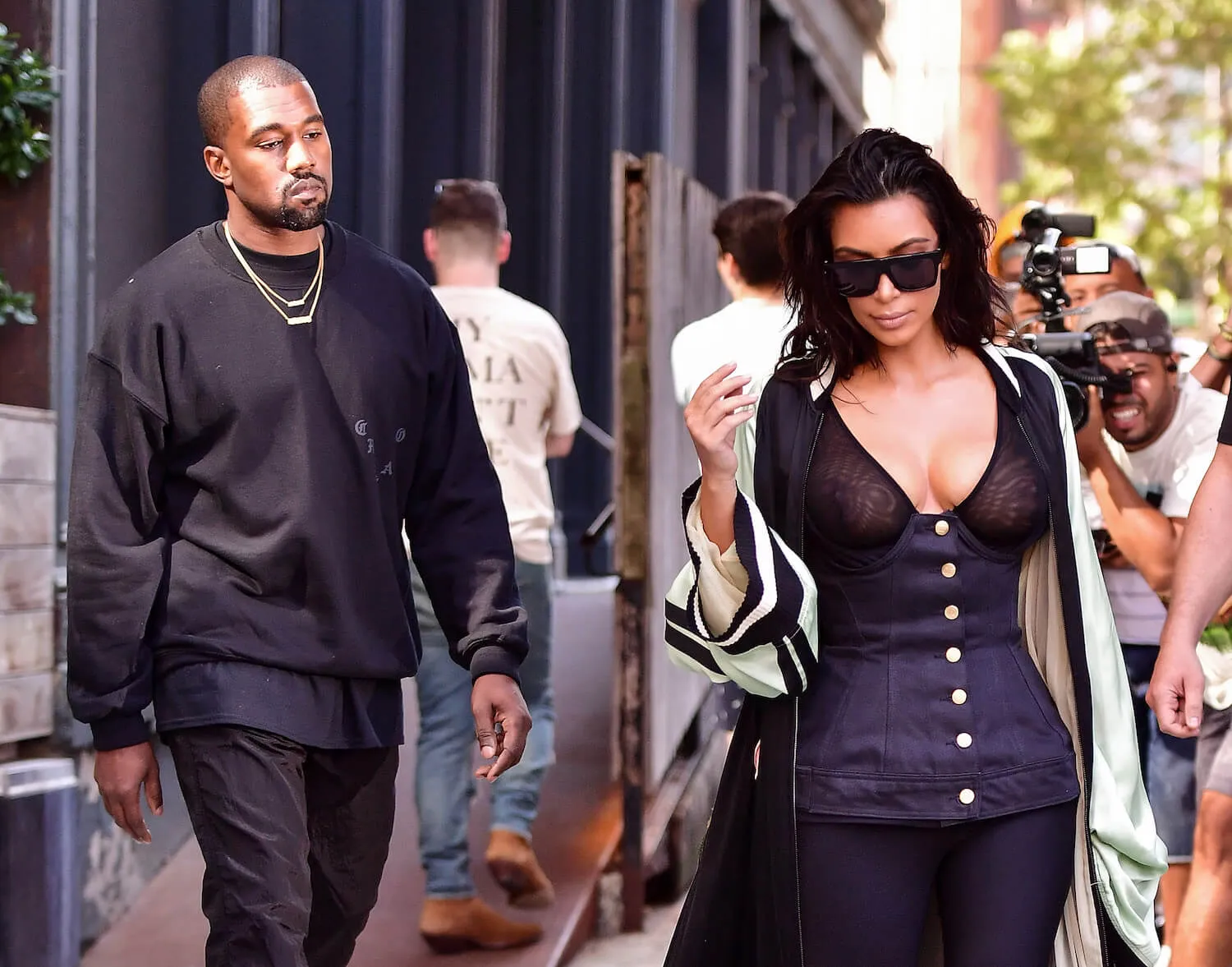 Kanye West and Kim Kardashian walking side by side in Manhattan in 2016. Kardashian is wearing a black corseted top and black sunglasses. West is wearing a black sweatshirt and black jeans.