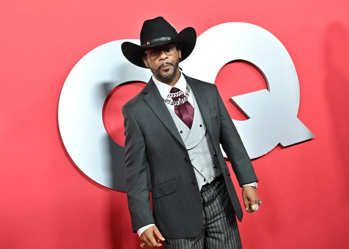 Wearing a gray coat with a purple ascot, Katt Williams poses for photos on the red carpet at the 2024 GQ Men Of The Year Party