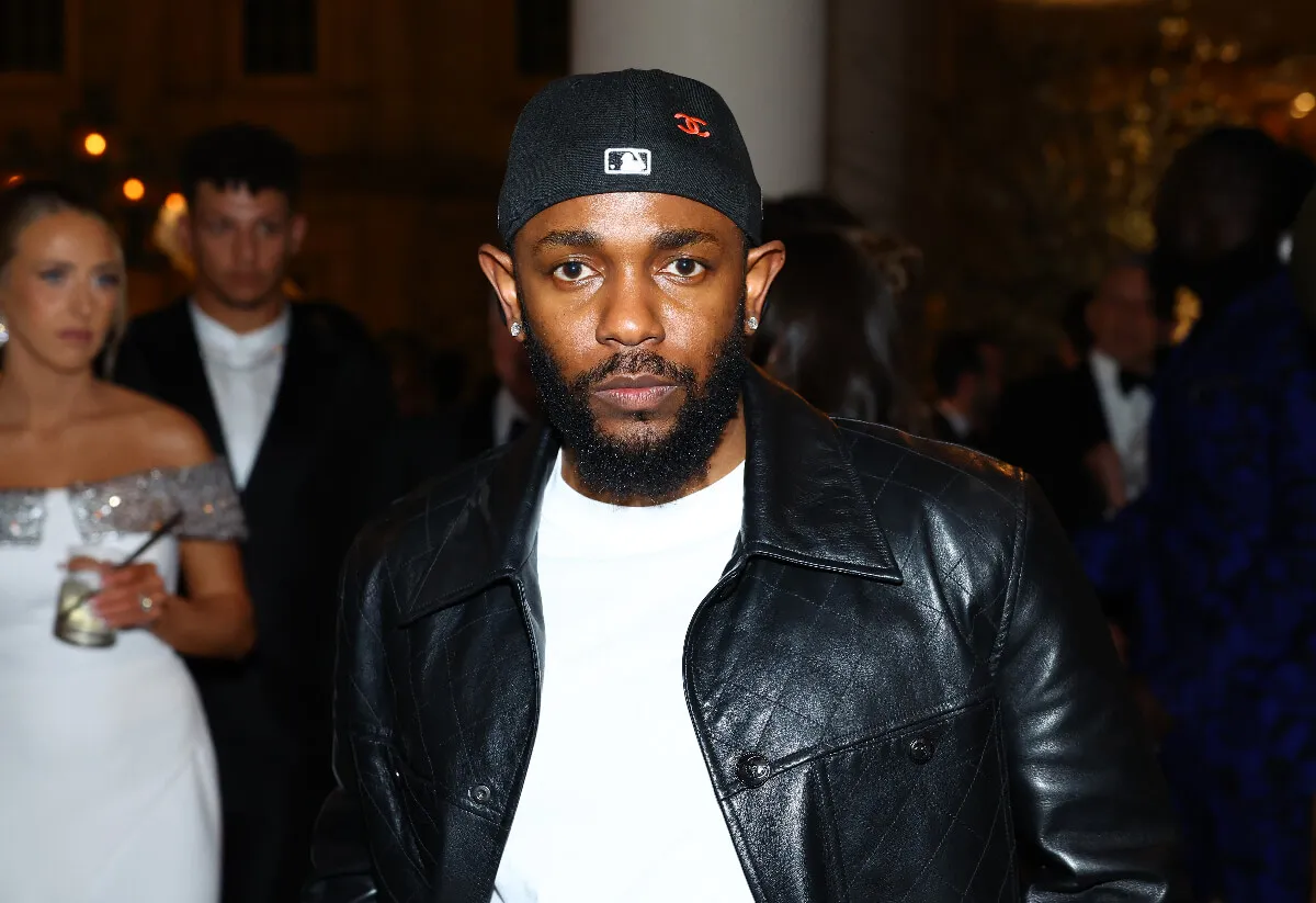 Kendrick Lamar wears a black leather jacket and a backwards baseball hat.