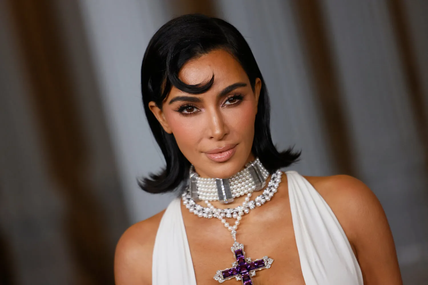 Kim Kardashian wearing a low-cut and sleeveless white dress with a large cross necklace at an event