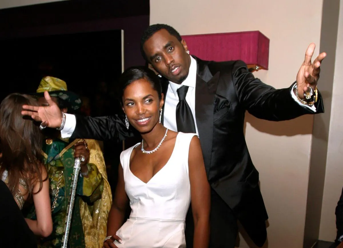 Kim Porter wears a white dress and stands in front of Sean 'Diddy' Combs, who wears a suit.