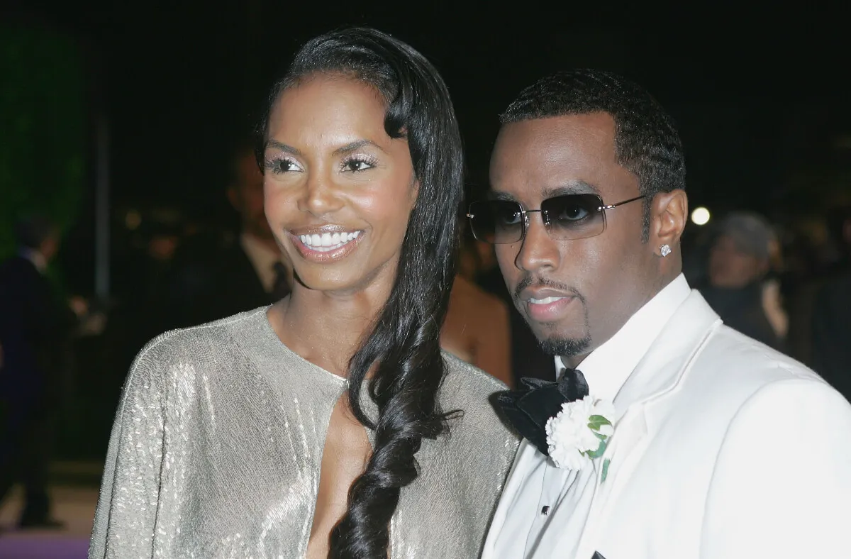 Kim Porter wears a silver dress and stands with Sean 'Diddy' Combs, who wears a white tuxedo and sunglasses.