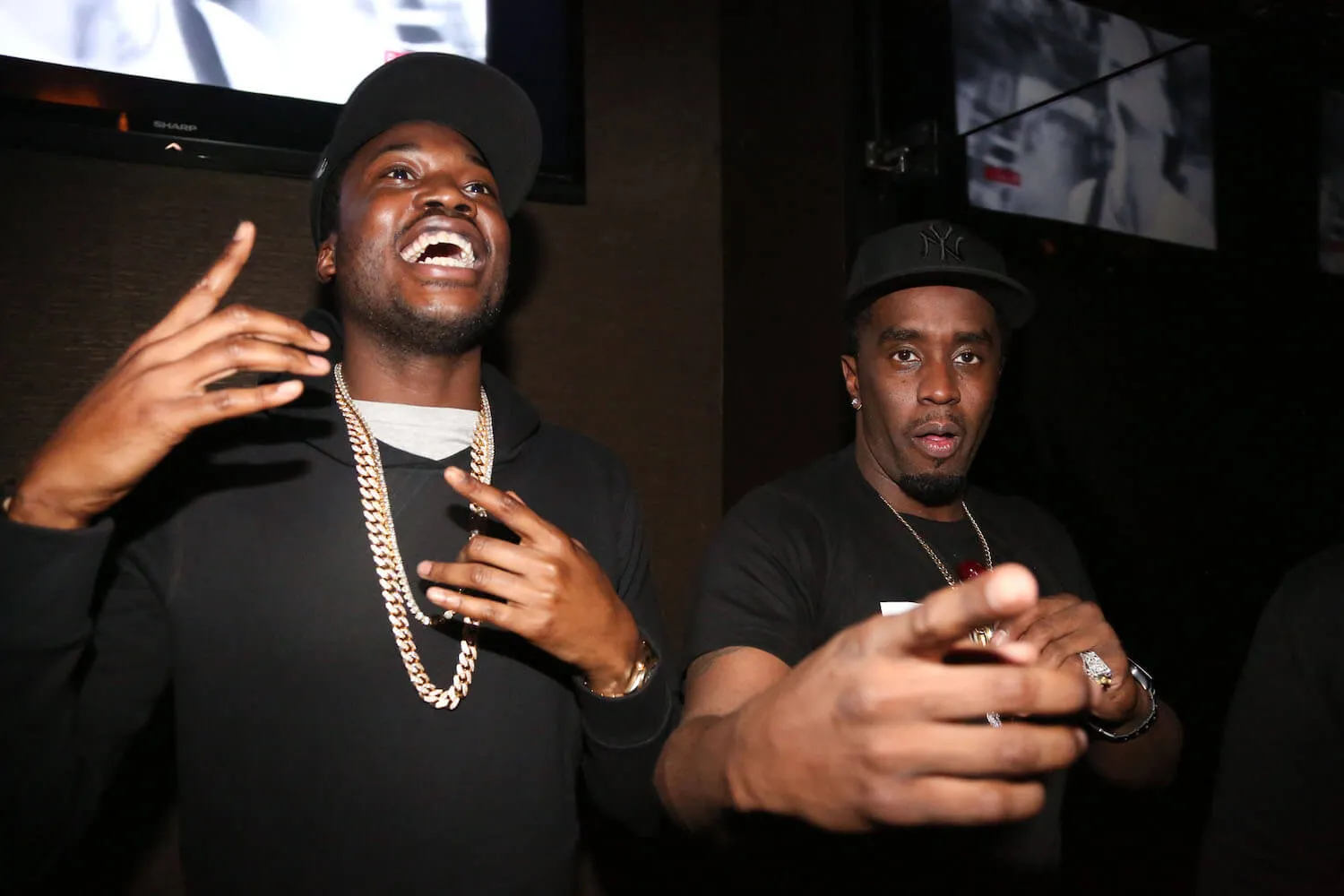 Meek Mill smiling and pointing up and Sean 'Diddy' Combs pointing at the camera against a black background at an afterparty 