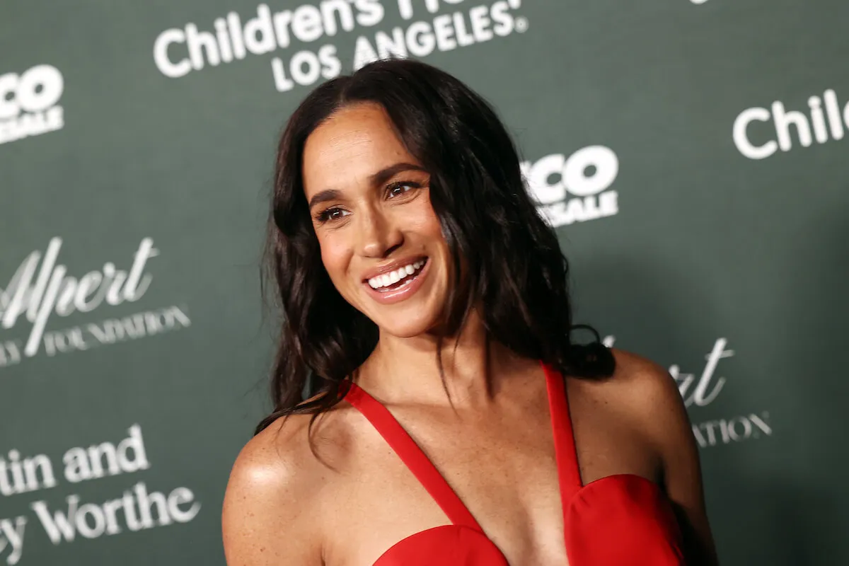 Meghan Markle, whose American Riviera Orchard lifestyle brand has yet to launch, smiles wearing a red gown.