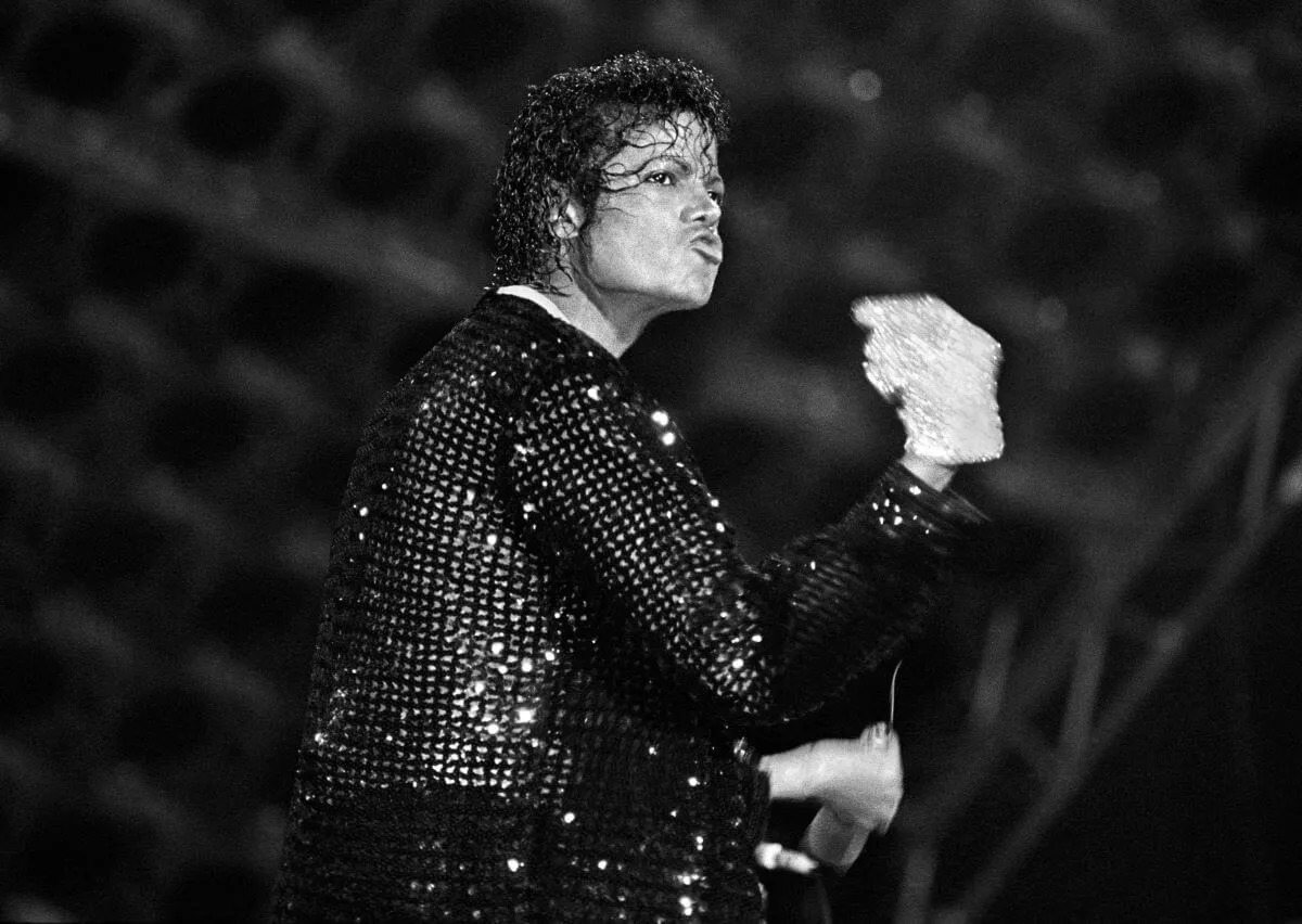 A black and white picture of Michael Jackson onstage. He wears a sequined jacket and gloves.