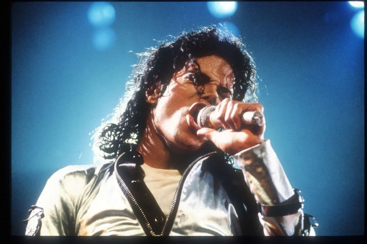 Michael Jackson sings into a microphone. He wears a silver jacket.