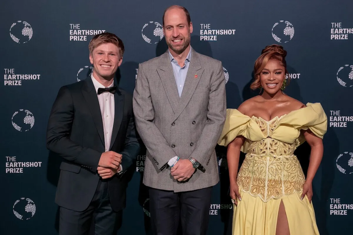 Prince William (center) wearing a blazer, dark pants and sneakers. He stands between Robert Irwin and Nomzamo Mbatha