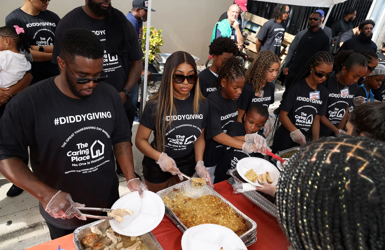 Yung Miami, Sean 'Diddy' Combs, and his family, his daughters Chance, D'Lila, and Jessie, standing next to each other and serving food as they celebrated Thanksgiving Day at The Caring Place in Miami on Nov. 24, 2022. They're all wearing "Diddygiving" black shirts.