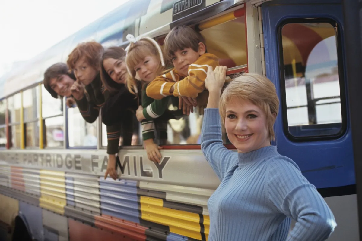 Shirley Jones standing in front of The Partridge Family bus with the kids' heads hanging out the windows