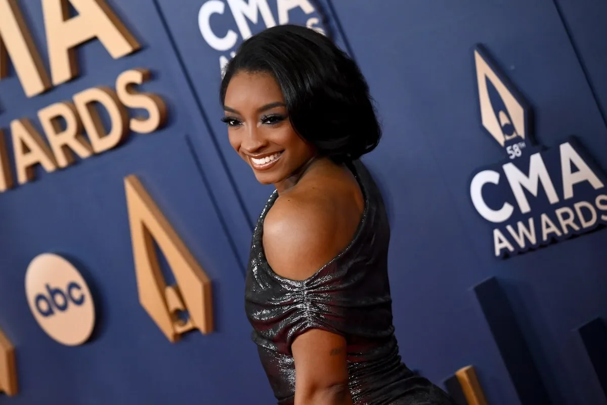 Wearing a silver gown, Simone Biles poses on the red carpet before the CMA Awards