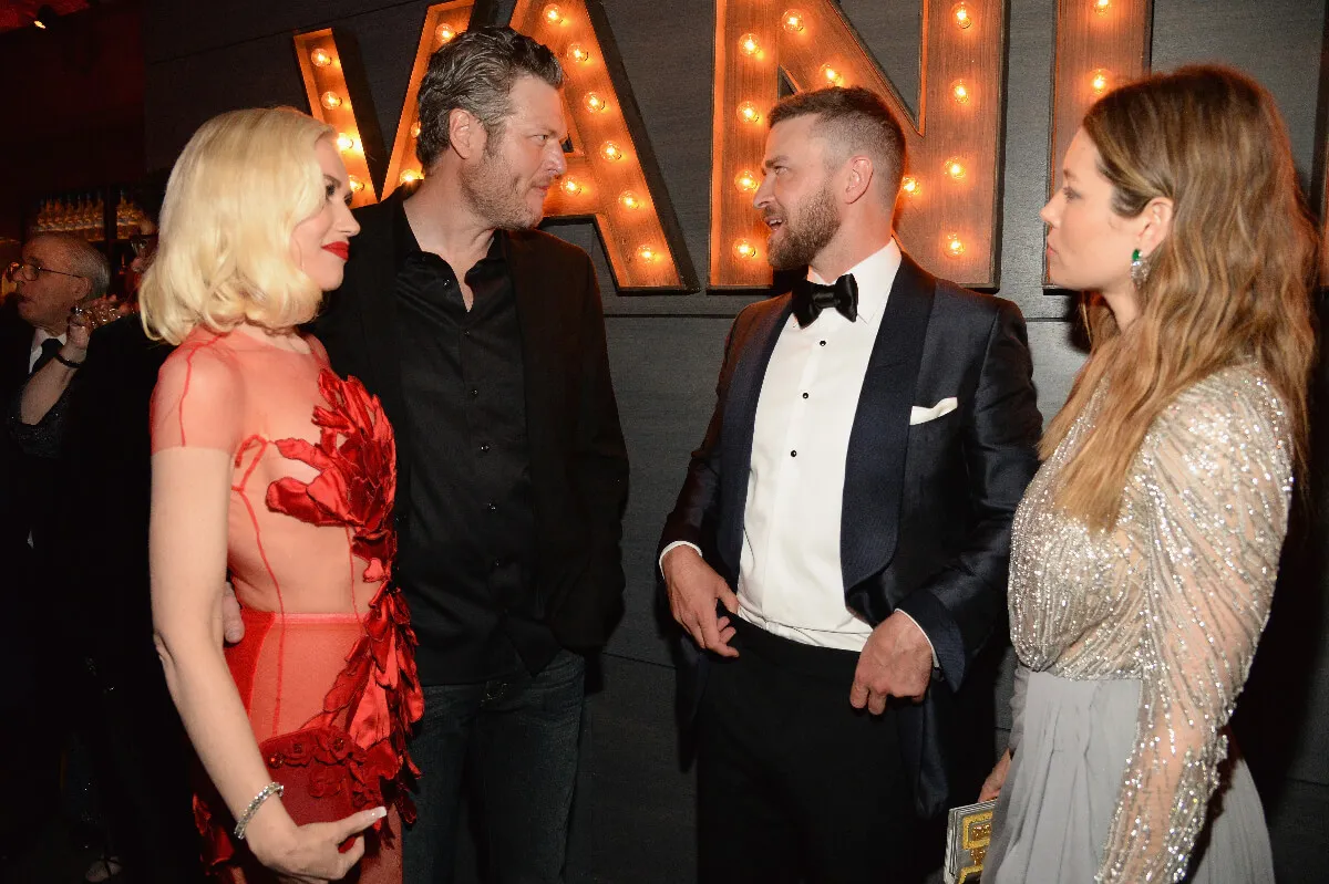 Gwen Stefani and Blake Shelton speak with Justin Timberlake and Jessica Biel. Stefani wears a red dress, Biel wears a silver dress, and Shelton and Timberlake wear suits.