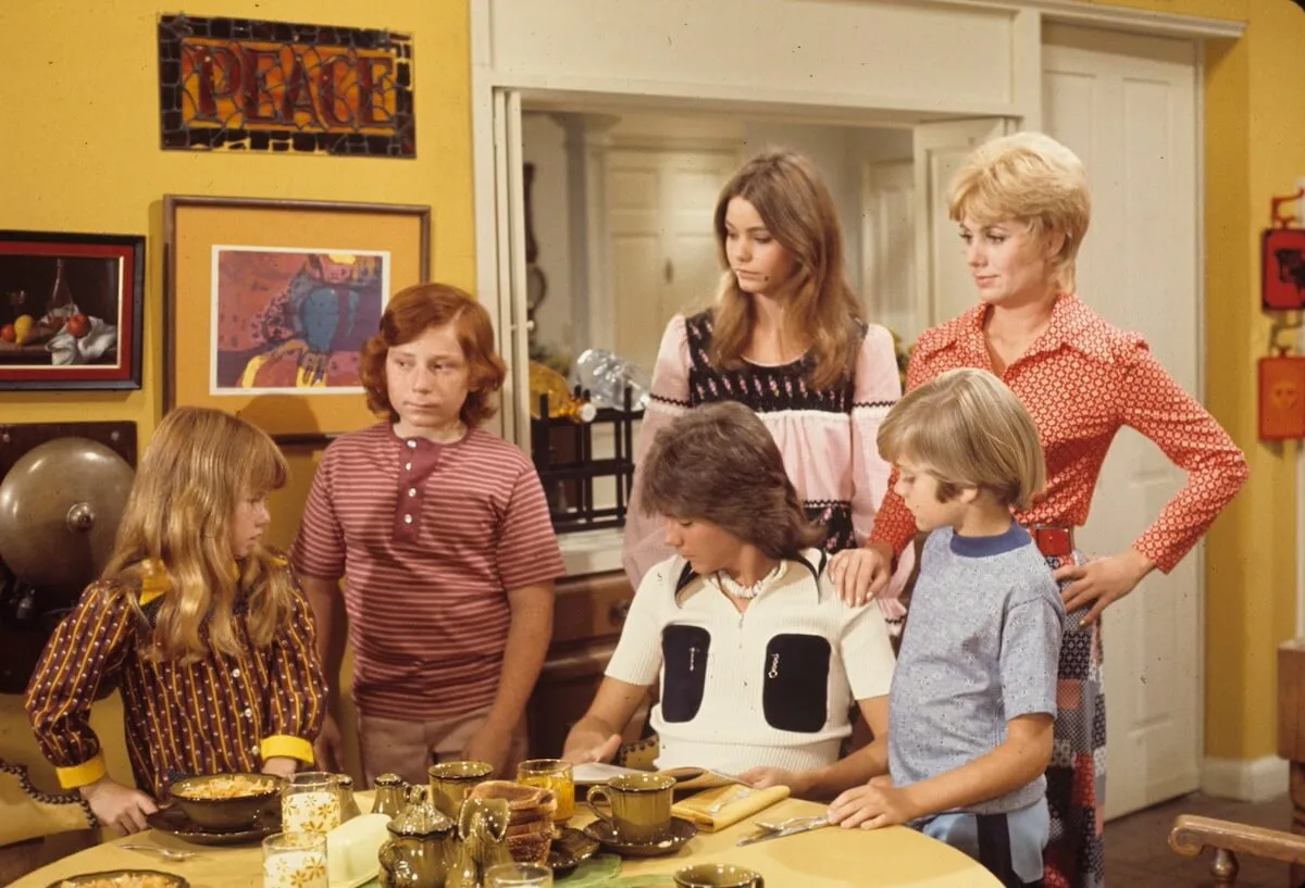 Members of the Partridge Family sitting and standing around a kitchen table