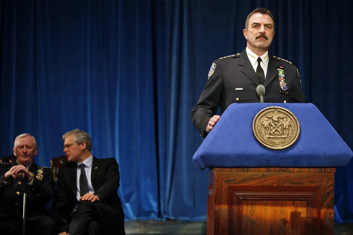 Tom Selleck as Frank Reagan standing behind a lectern in 'Blue Bloods'