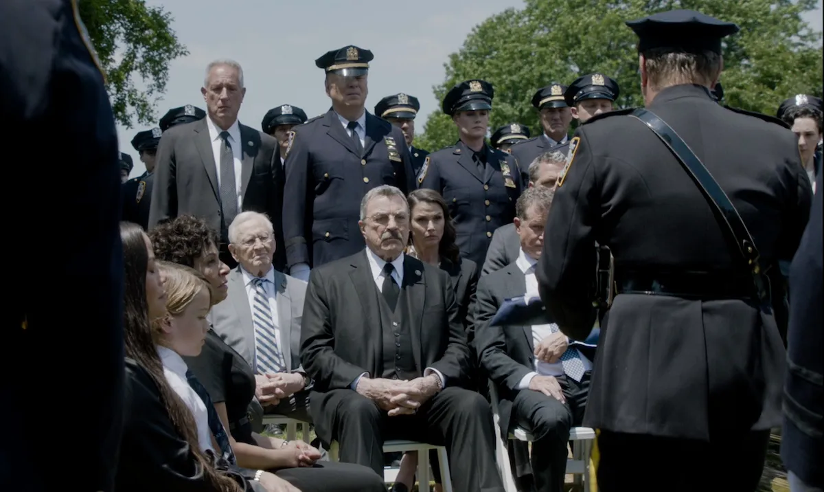 Tom Selleck, center, sits surrounded by other cops in dress uniform at a funeral in the 'Blue Bloods' Season 14 finale