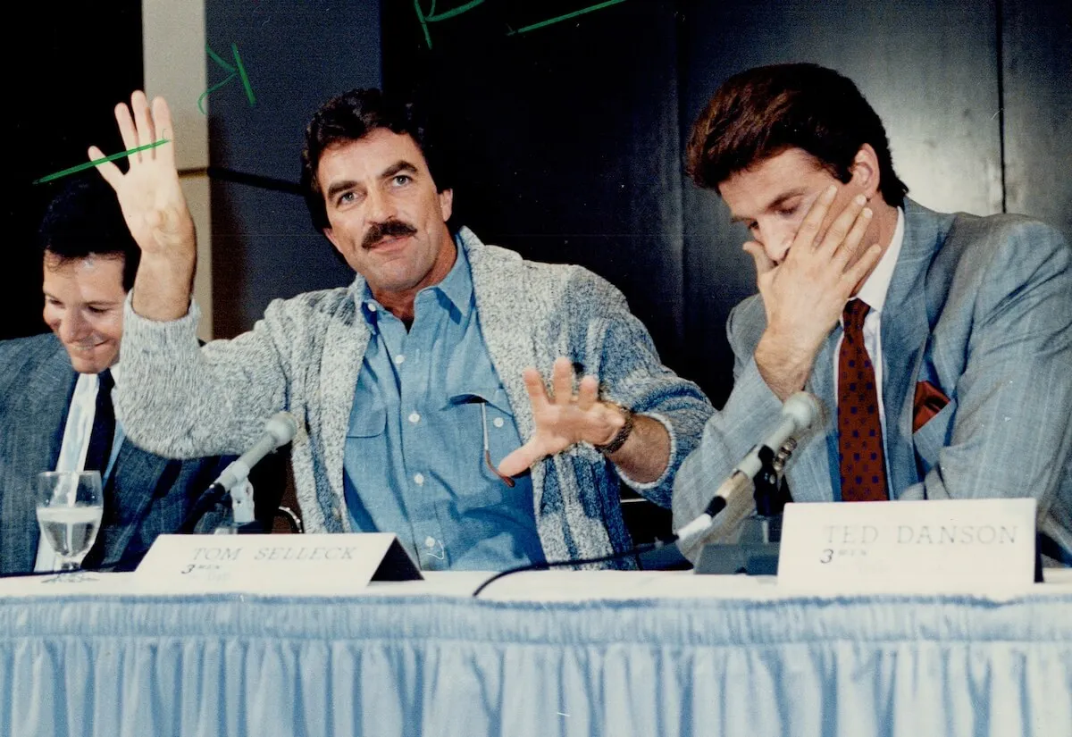 Tom Selleck sitting at a table at a press conference between Steve Guttenberg and Ted Danson