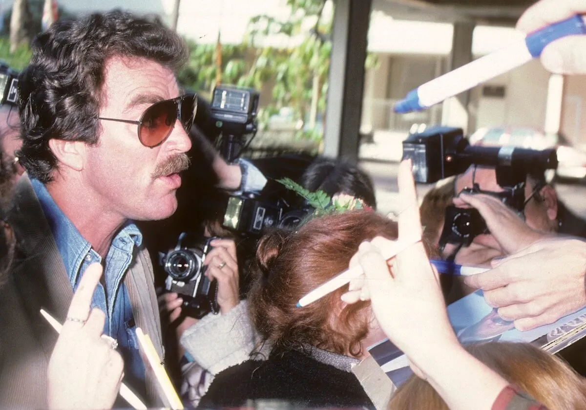 Tom Selleck, wearing sunglasses, with microphones in his face