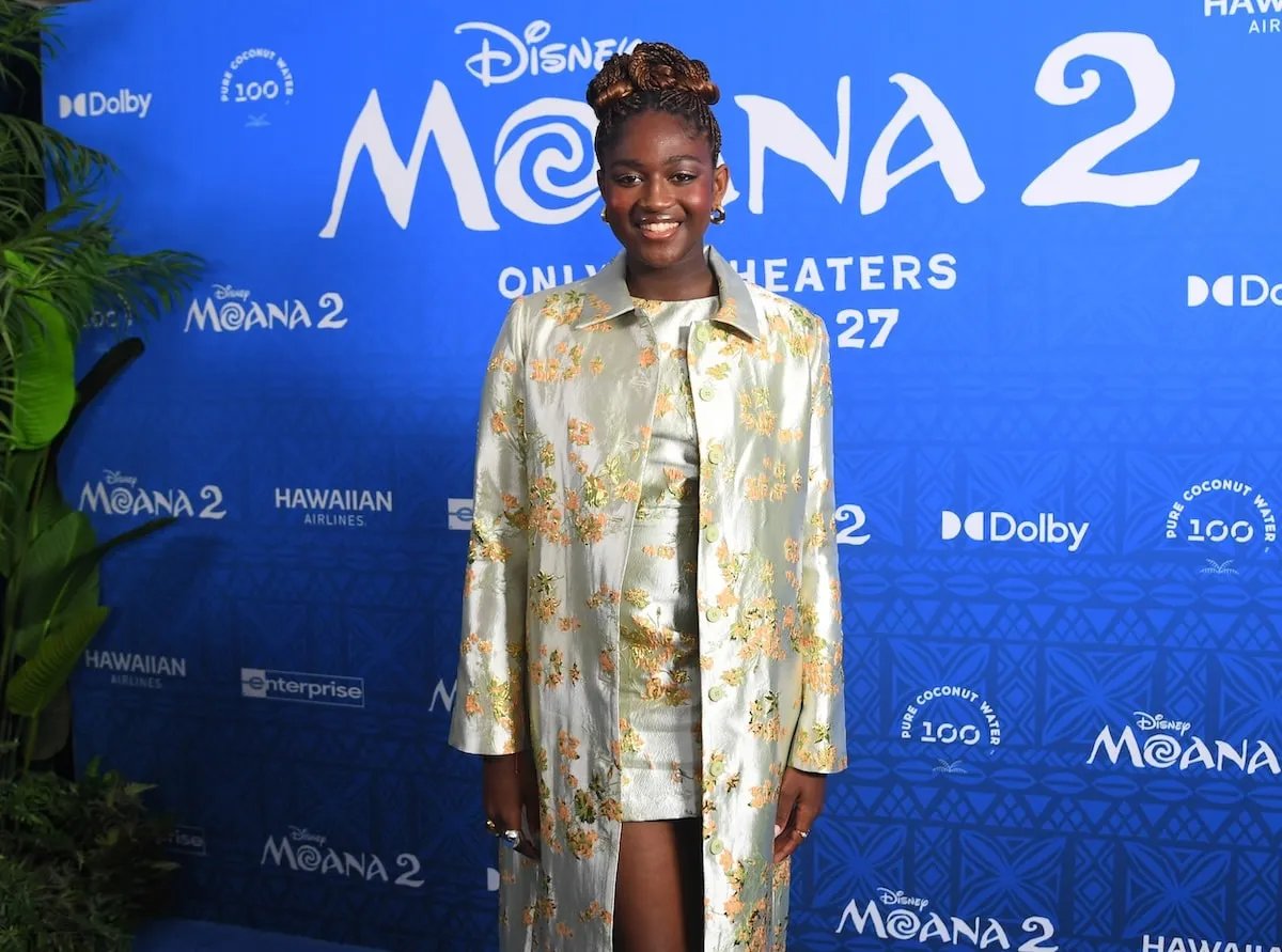 Wearing a brocade mini dress and coat, Zaya Wade smiles on the red carpet before the Moana 2 premiere