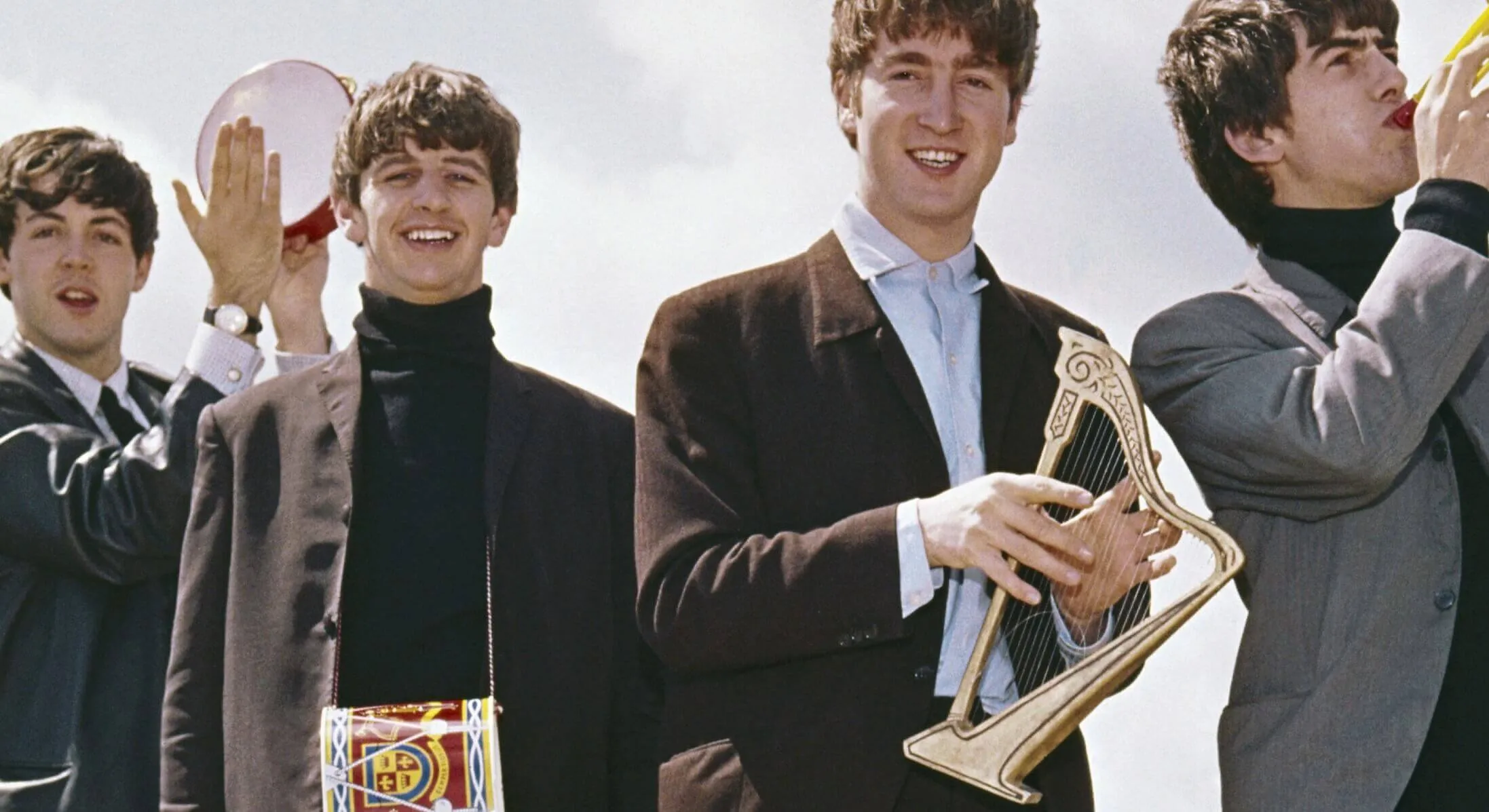 The Beatles stand on a rooftop holding small versions of instruments.