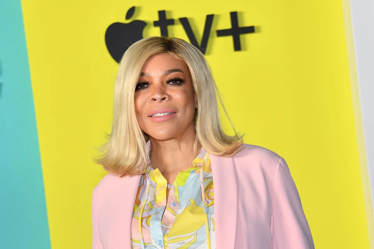 Wendy Williams posing at Apples Apples "The Morning Show" wearing a pink sweater and a yellow and blue shirt.