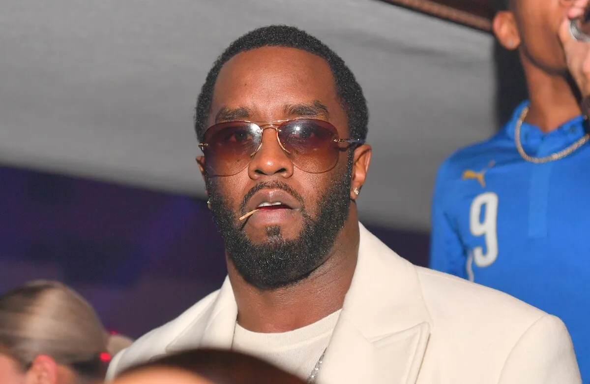 Sean Diddy Combs posing in a white blazer and t-shirt while chewing on a toothpick at The Official Big Game Take over.