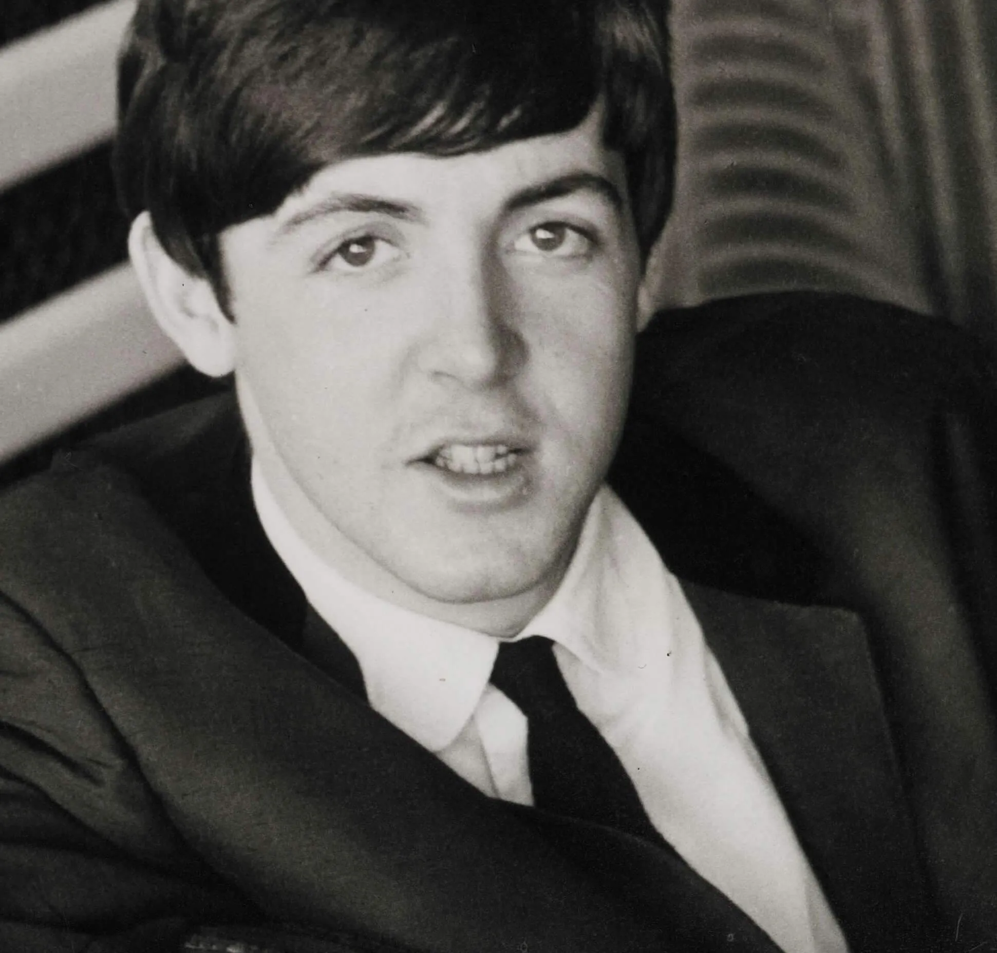 Paul McCartney wears a suit and sits in a chair.