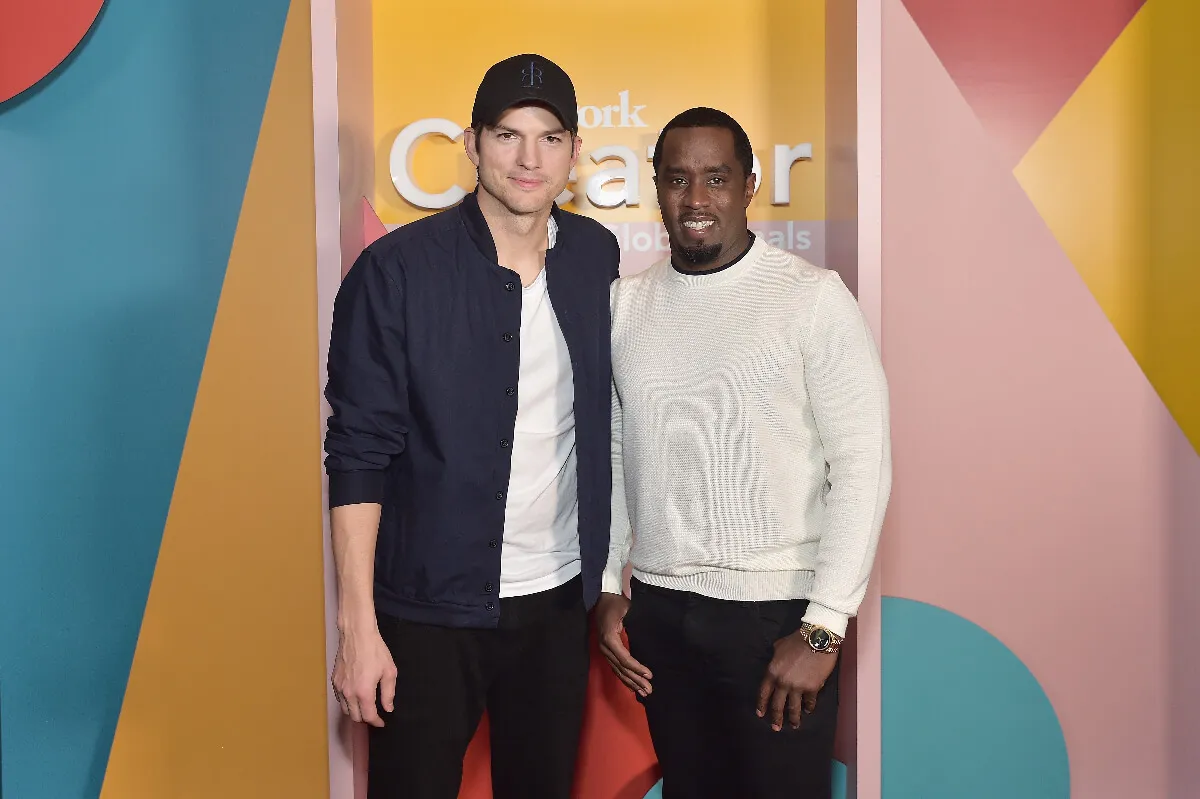 Ashton Kutcher and Sean 'Diddy' Combs stand together. Kutcher wears a baseball hat.