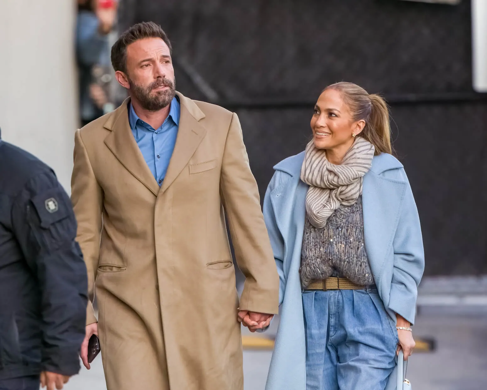 Ben Affleck in a camel coat and Jennifer Lopez in a blue coat walking hand in hand in December 2021