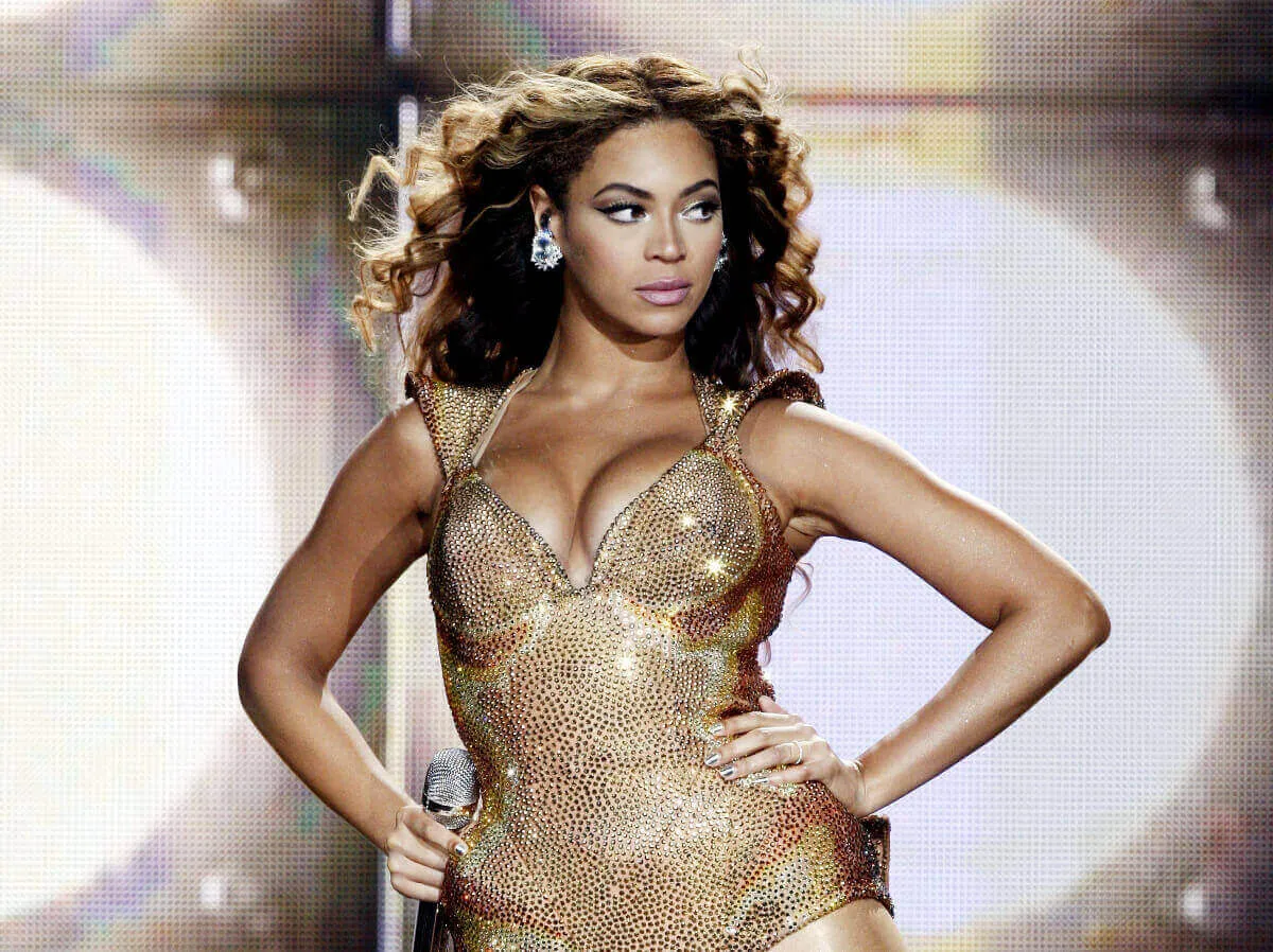 Beyonce wears gold sequins and stands on stage with her hands on her hips.