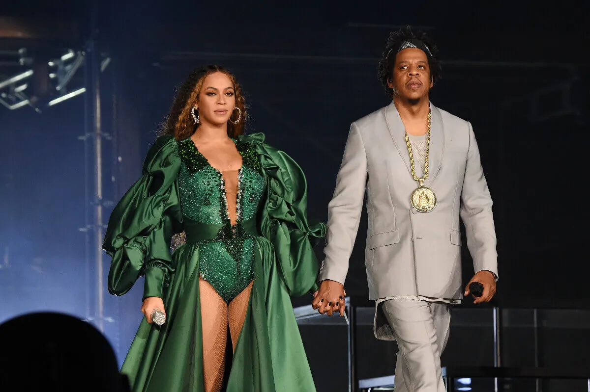 Beyoncé wears a green costume and holds hands with Jay-Z, who wears a gray suit.