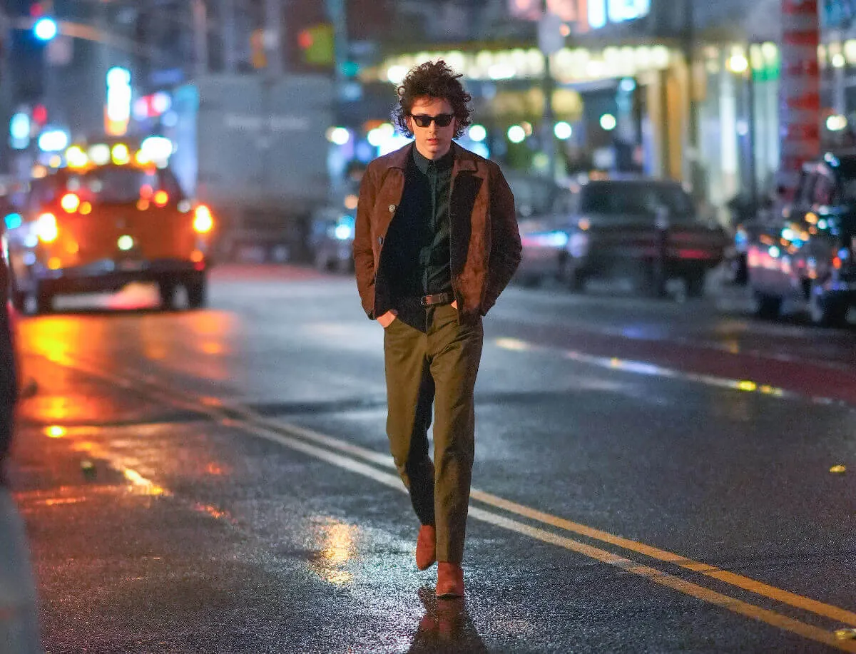 Timothée Chalamet walks in the street while playing Bob Dylan.