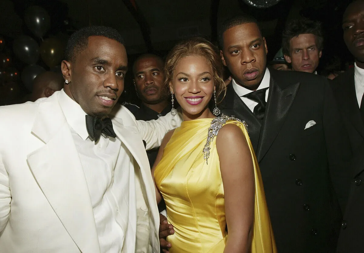 Sean 'Diddy' Combs wears a white suit and stands with Beyonce, who wears a yellow dress, and Jay-Z who wears a black suit.