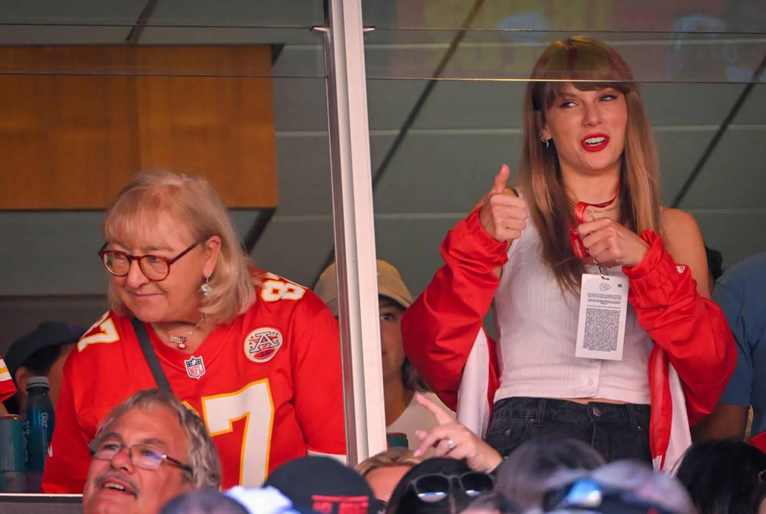 Donna Kelce sitting next to Taylor Swift, who's gesturing and standing, at a Kansas City Chiefs game