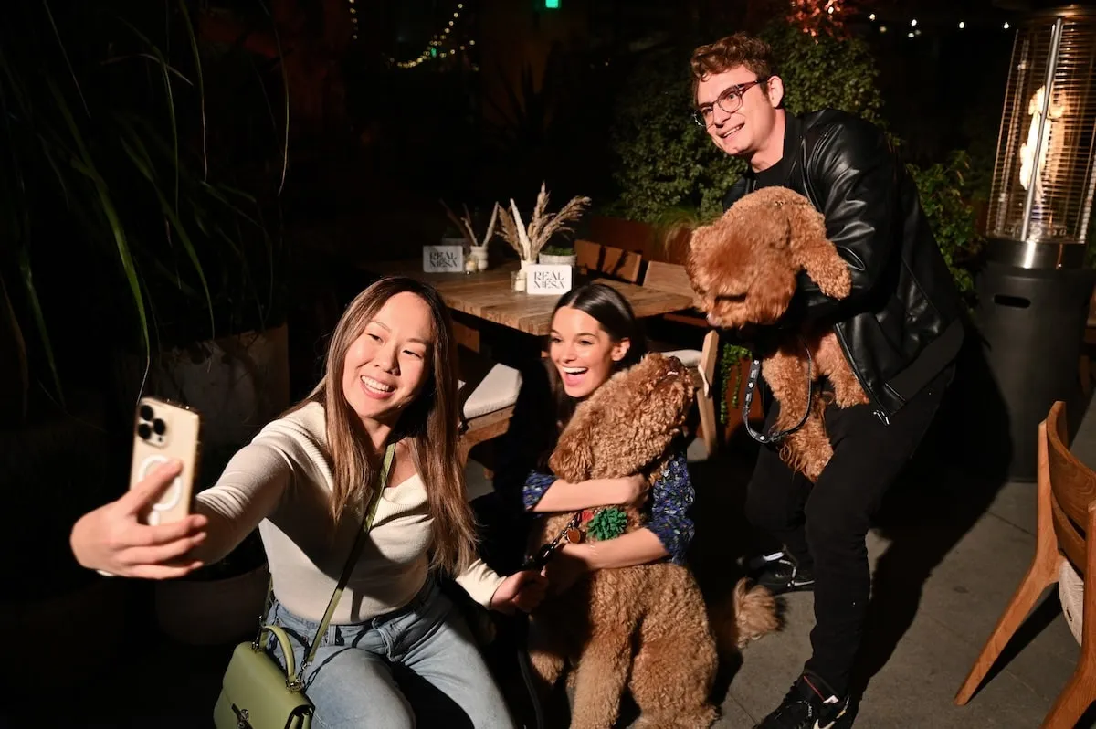 Smiling together, Ally Lewber and James Kennedy take photos with their goldendoodle Hippie at Dogsgiving with REÁL MESA