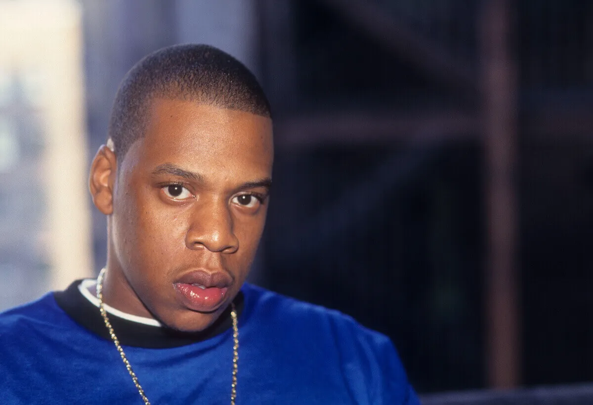 Jay-Z wears a blue shirt and sits by a window.